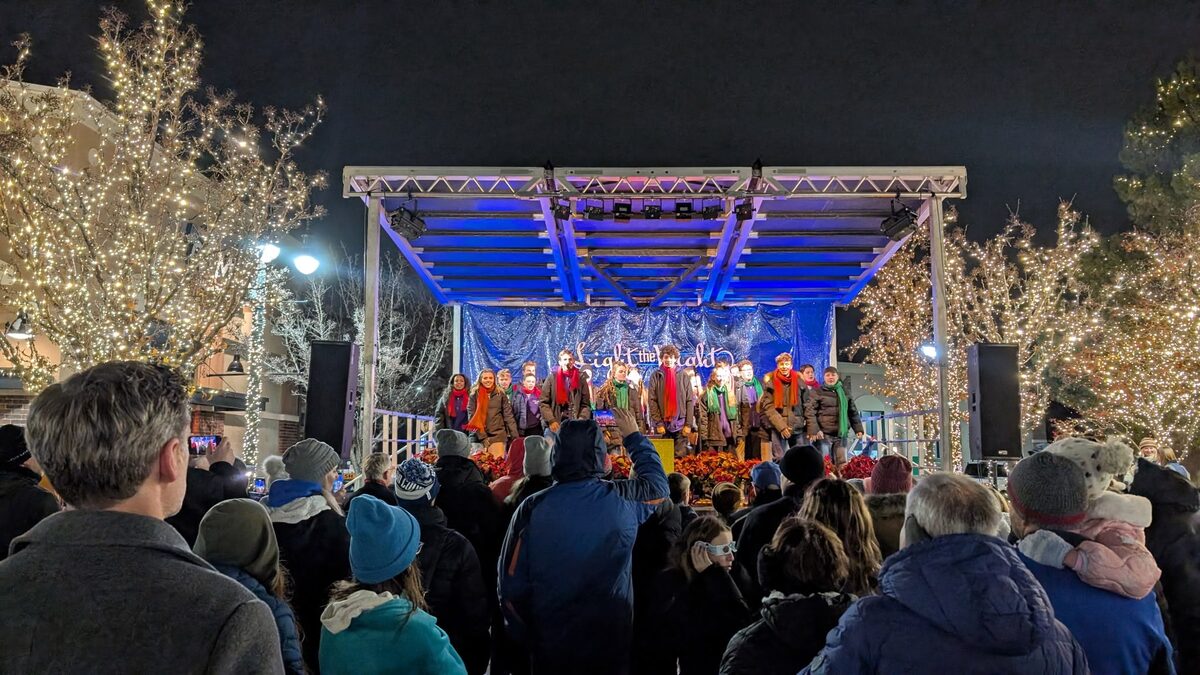 A crowd watching a blue-lit outdoor stage among tree-lit plaza lights at a community tree-lighting night