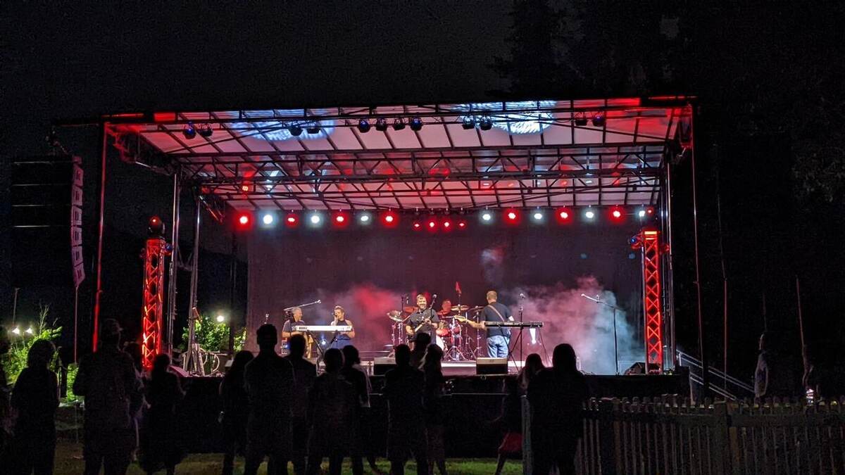 A band performing on a night outdoor stage bathed in vivid red and blue stage lighting with haze, silhouetted audience watching