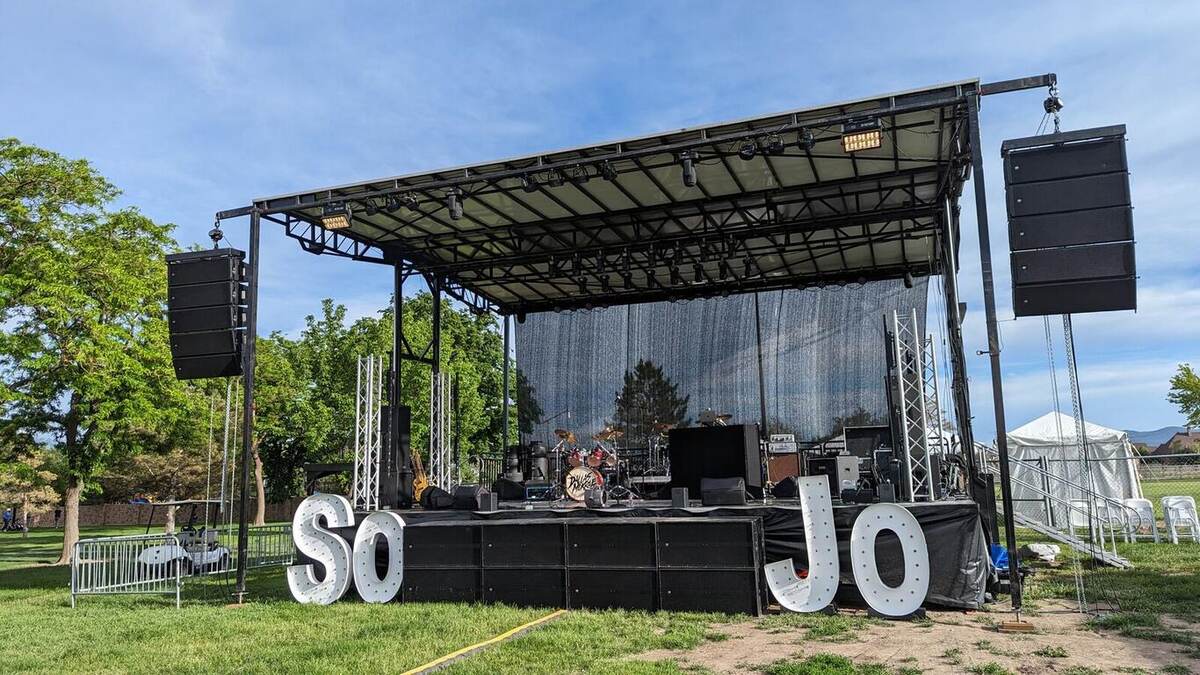 A large black outdoor mobile stage with roof, line-array speakers, and backline set up on grass, with giant illuminated 'SoJo' marquee letters in front