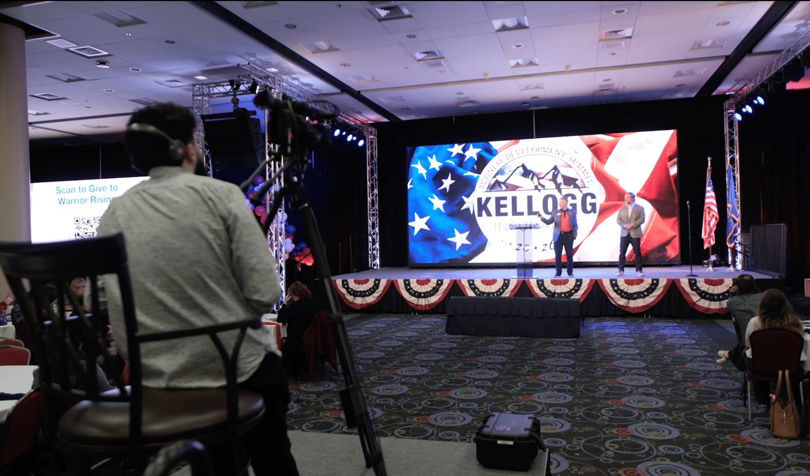 A True AV camera operator filming the Kellogg summit main stage, framed by the branded LED wall and stage lighting